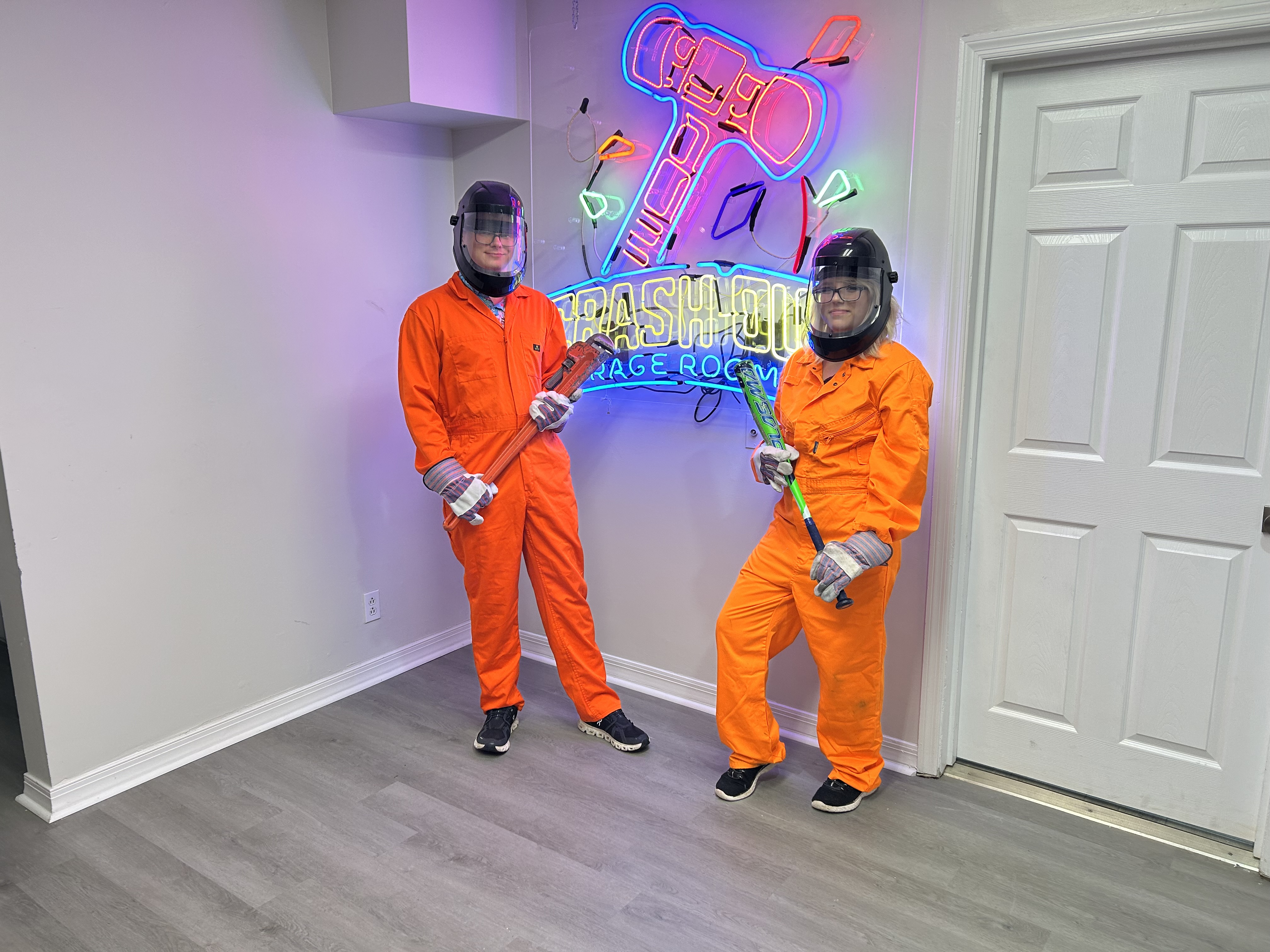 Group of Crash Out customers in orange jumpsuits holding bats in front of neon sign